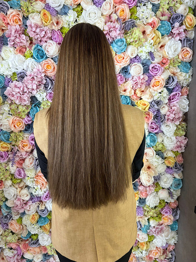 Lang, glanzend bruin haar voor de bloemenmuur